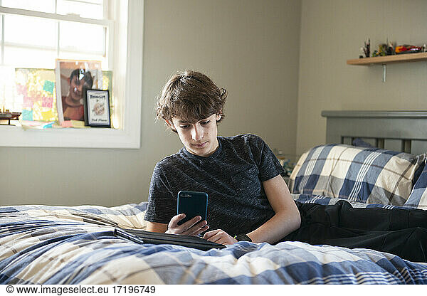 Tween boy laying on bed with phone and tablet.
