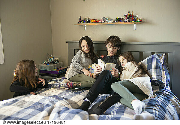 Tween boy reading to his little sisters in bedroom.