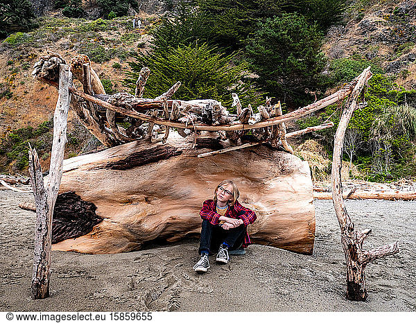 Tween boy sitting in driftwood structure at the beach