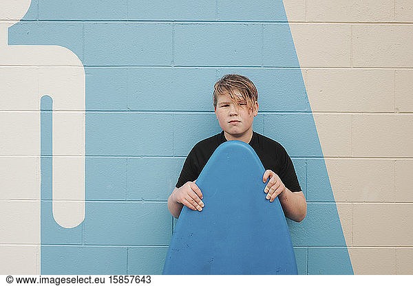 Tween boy standing against wall holding a boogie board