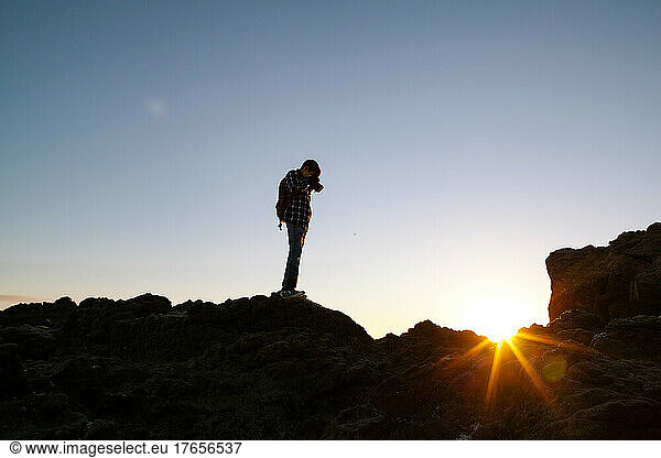 Tween Boy Stands Backlit On A Rock While Taking A Picture