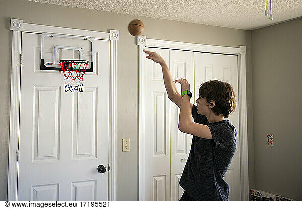 Tween boy throwing a small basketball in his bedroom.