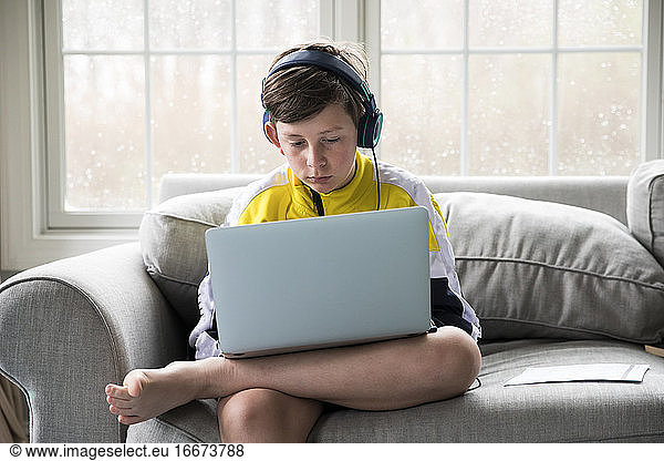 Tween Boy Using Laptop for Virtual School Sits on Living Room Couch