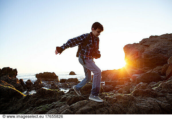 Tween Boy Walks On Rocks At Beach While Holding Camera