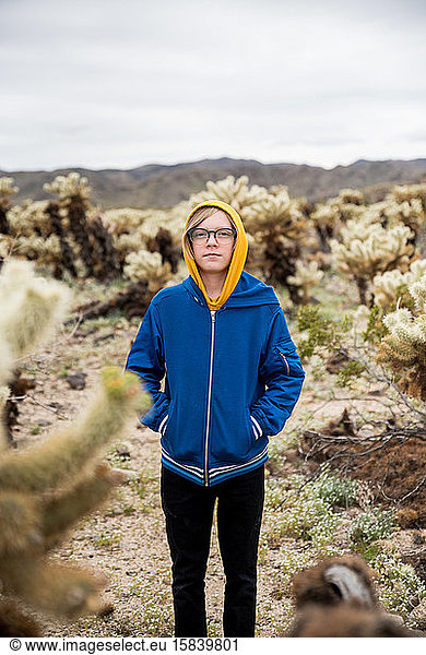 Tween boy with glasses in desert surrounded by cholla cacti by hills