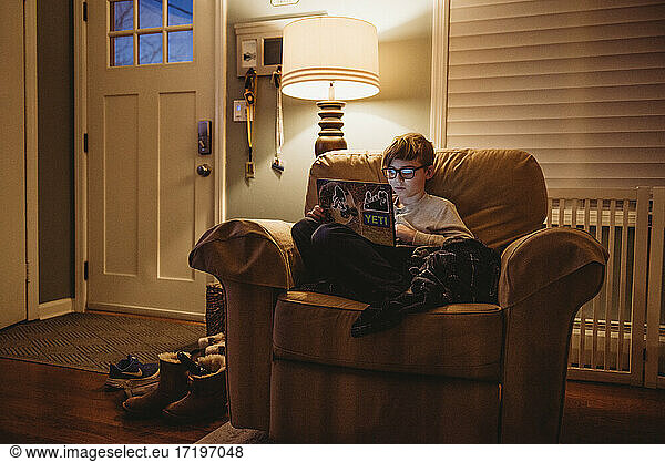 Tween boy working on laptop at home in large chair
