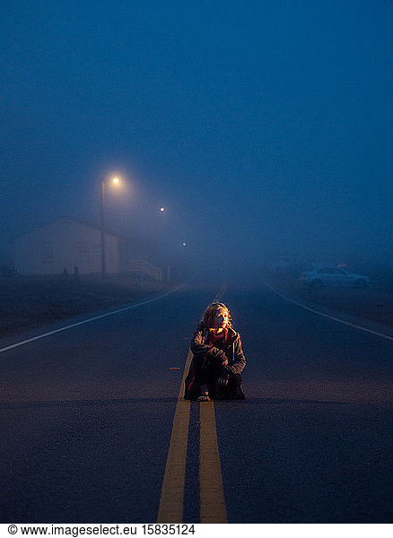 Tween crouching in roadway on foggy evening