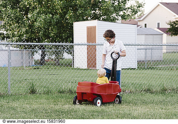 Tween  der ein Kleinkind in einem Wagen im Hinterhof zieht.
