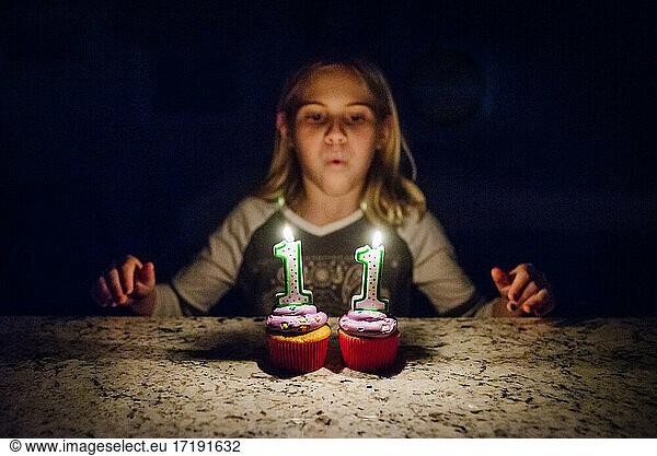 Tween girl blowing out candles on two cupcakes with face not in focus