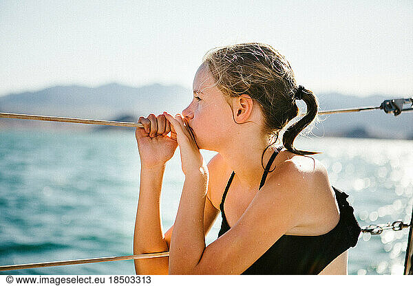 Tween girl in swimsuit on edge of boat overlooking water in sunshine