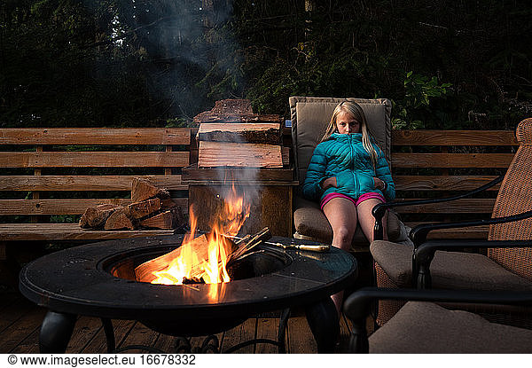 Tween Girl Sitting ruhig in der Nähe von Outdoor-Feuerstelle in der Abenddämmerung