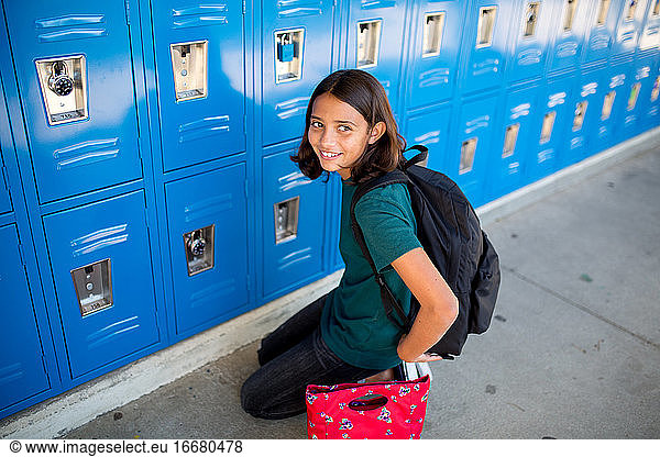 Tween girl smiles in front of her locker at middle school