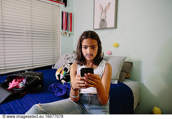 Tween girl takes a serious selfie while wearing a painted on mustache