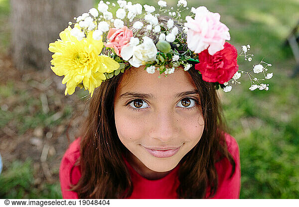 Tween girl with live flower head wreath looks up at camera