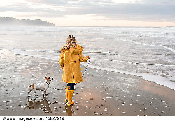 Tween in yellow coat walking dog at beach in New Zealand