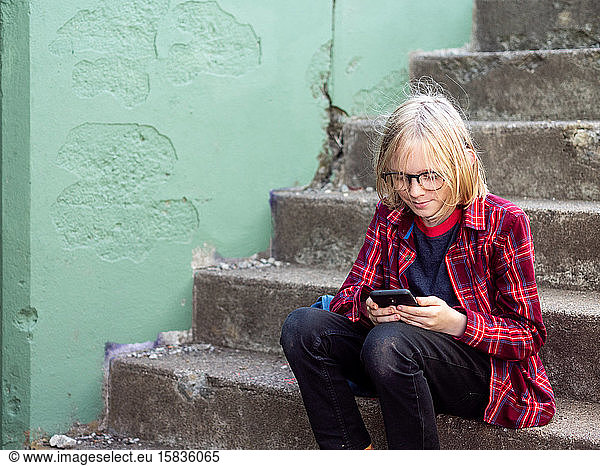 Tween smiling sitting on stairs using smartphone