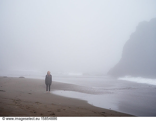 Tween standing alone on a beach in fog