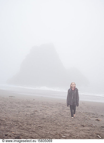Tween walking away from ocean across foggy beach