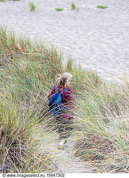 Tween walking away toward beach through tall sea grass