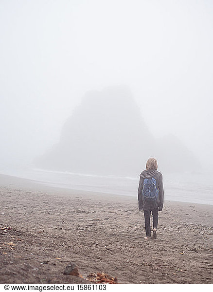 Tween walking toward ocean across foggy beach