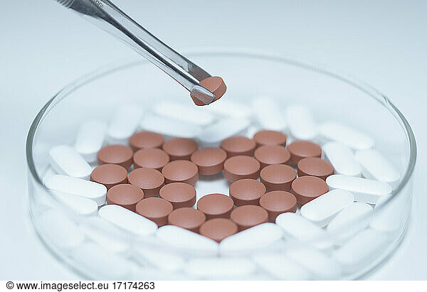 Tweezers holding a pill over a Petri dish with generic pills forming heart symbol