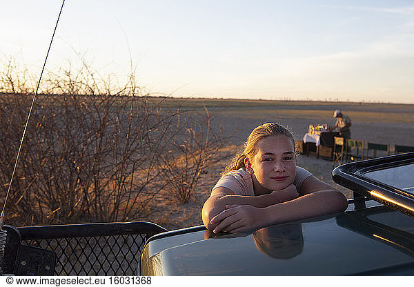 Twelve year old girl leaning on the roof of a jeep in the Kalahari Desert at sunset.