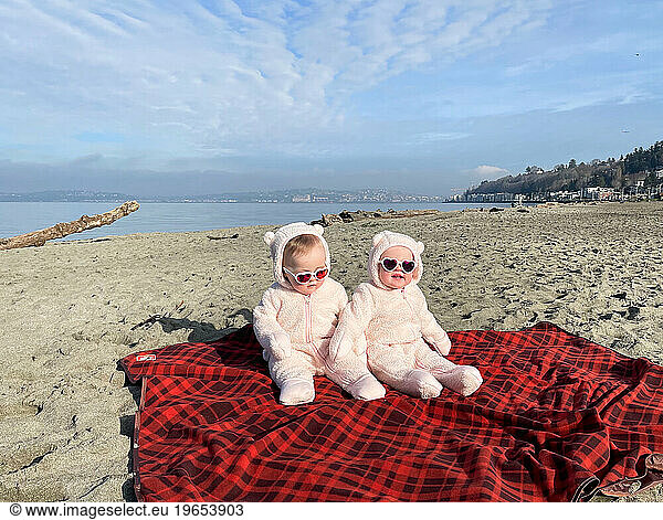 Twin baby girls in pink bear onesies on the beach