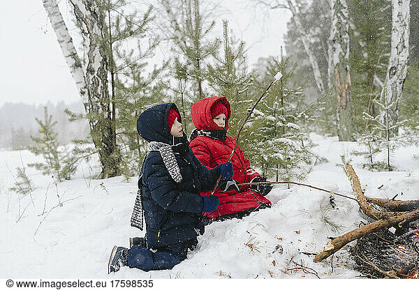 Twin brothers roasting marshmallows in bonfire at snowy forest