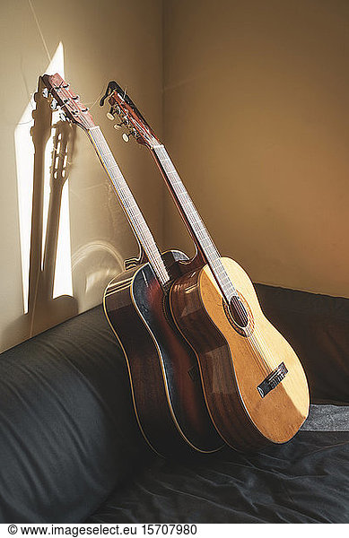 Two acoustic guitars leaning on couch at sunlight