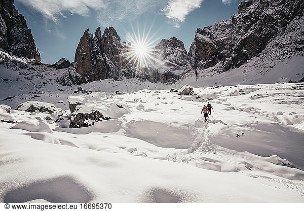 Two alpinists descending on snowy trail against sun rays in Dolomites