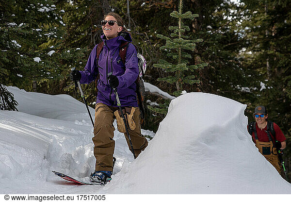 Two backcountry snowboarders skinning through a snowy forest