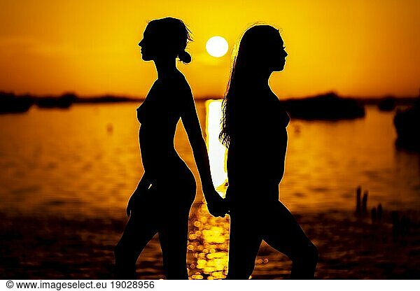 Two beautiful nude latin models are silhouetted against the rising sun behind them on a exotic Caribbean beach