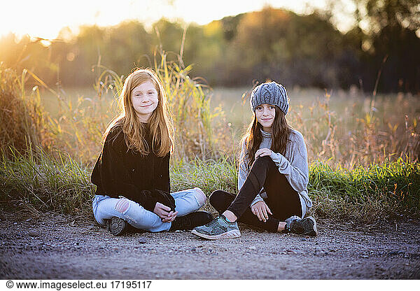Two beautiful young tween girls sitting outdoors in fall  backlit.