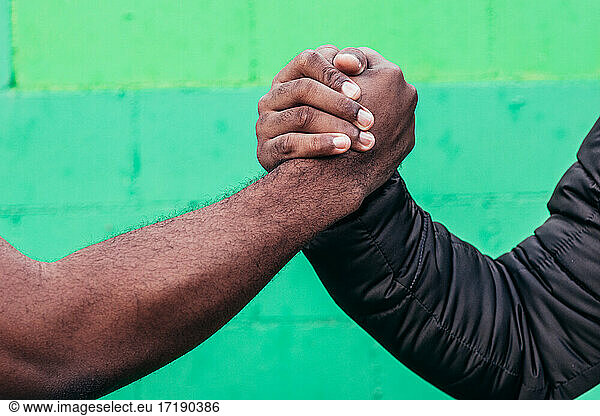 Two black boys shaking hands. Close up of hands on green wall background.