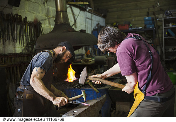 Two blacksmiths hammer a piece of metal on an anvil in a workshop