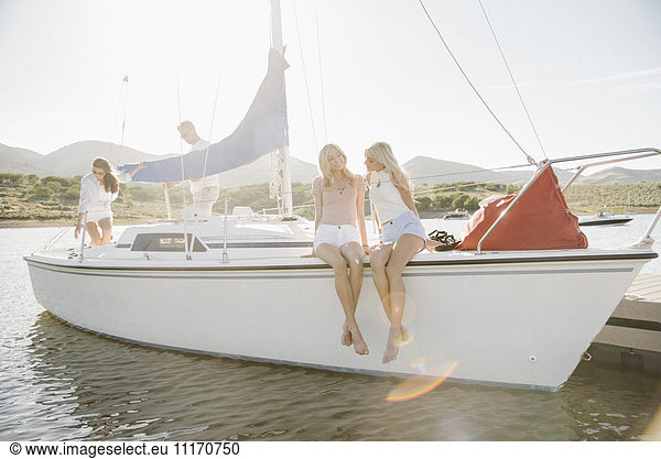 Two blond sisters sitting on a sail boat.