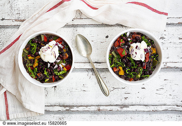 Two bowls of black bean soup with bell pepper  cilantro  sour cream and red onions