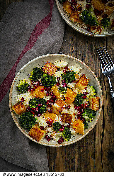 Two bowls of couscous with broccoli  halloumi cheese  oranges  chili dressing and pomegranate seeds