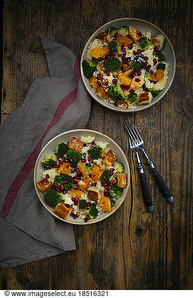 Two bowls of couscous with broccoli  halloumi cheese  oranges  chili dressing and pomegranate seeds