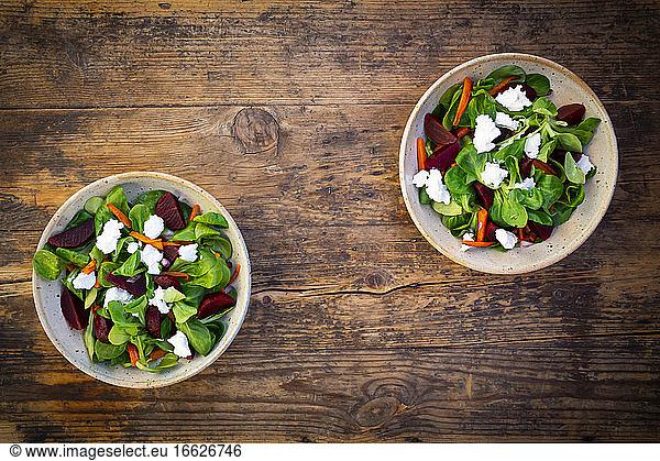 Two bowls of vegetarian salad with roasted carrot strips beetroot corn salad goat cheese and Spanish onions