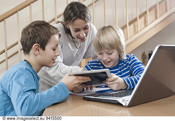 Two boys and female childcare assistant with laptop and tablet computer