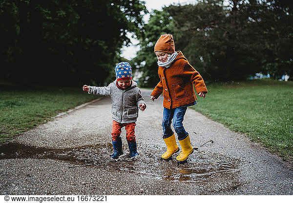 Two boys jumping in the puddles at the park on cloudy day