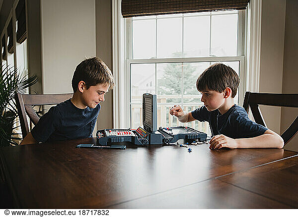 Two boys playing a board game together at a wooden table.