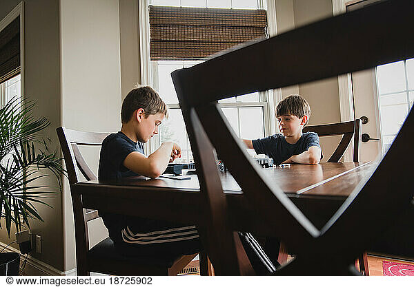 Two boys playing a board game together at a wooden table.