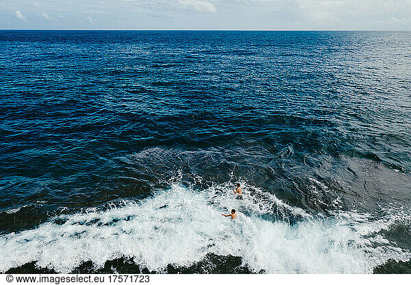 Two boys playing in the waves on the edge of the blue ocean