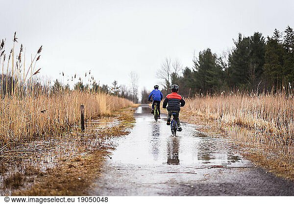 Two boys riding their bikes through a large puddle on a flooded trail.