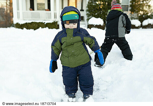 Two boys stand in snow in front yard during winter wearing winter gear