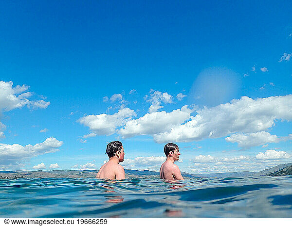 Two Boys Swimming In Lake with Blue Sky and Blue Water