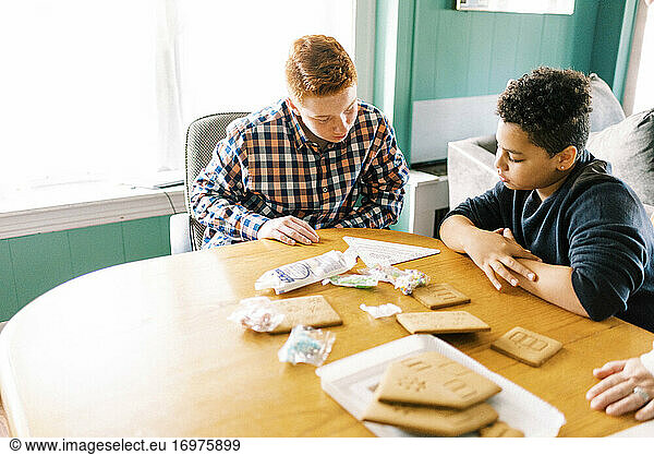 Two brothers building a gingerbread house during christmas time