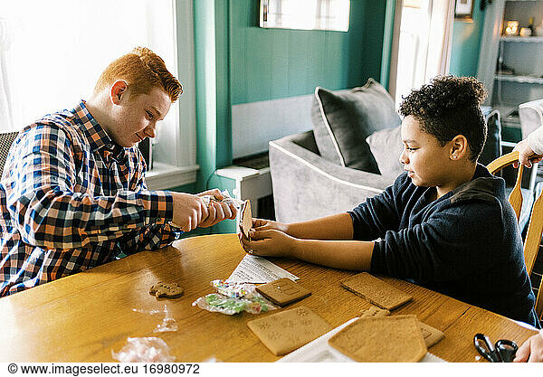 Two brothers making a gingerbread house together in the living room